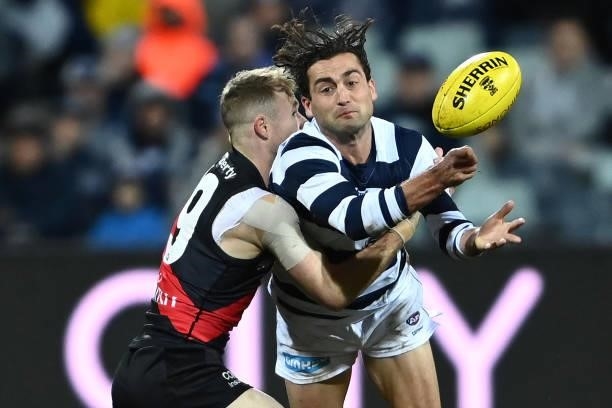 Luke Dahlhaus of the Cats handballs whilst being tackled by Nick Hind of the Bombers during the round 16 AFL match between Geelong Cats and Essendon...