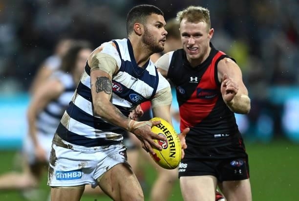 Brandan Parfitt of the Cats kicks whilst being tackled by Nick Hind of the Bombers during the round 16 AFL match between Geelong Cats and Essendon...