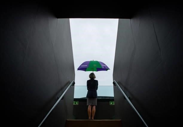 Steward shelters under an umbrella as rain stops play on No.3 Court during Day Six of The Championships - Wimbledon 2021 at All England Lawn Tennis...