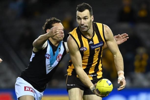 Jonathon Ceglar of the Hawks handballs whilst being tackled by Steven Motlop of the Power during the round 16 AFL match between Hawthorn Hawks and...
