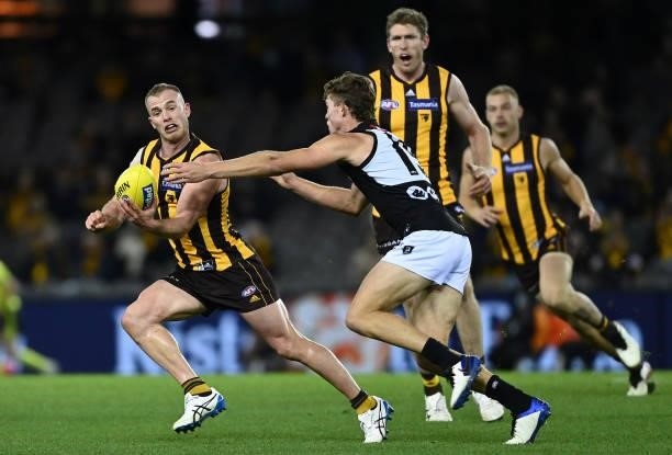 Tom Mitchell of the Hawks handballs whilst being tackled by Mitch Georgiades of the Power during the round 16 AFL match between Hawthorn Hawks and...