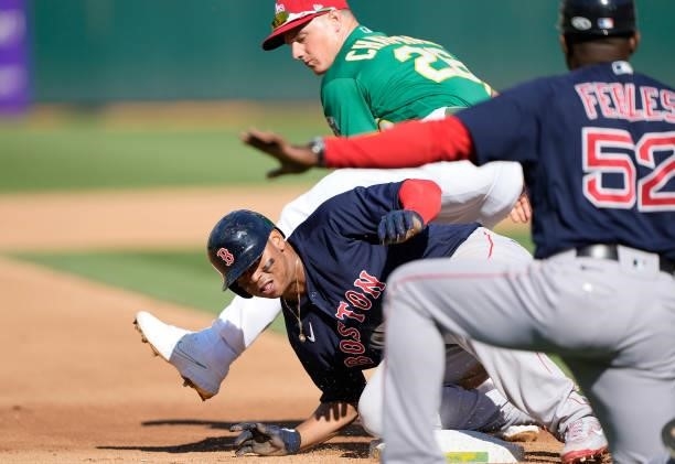 Rafael Devers of the Boston Red Sox slides safely under Matt Chapman of the Oakland Athletics into third base in the top of the fourth inning at...