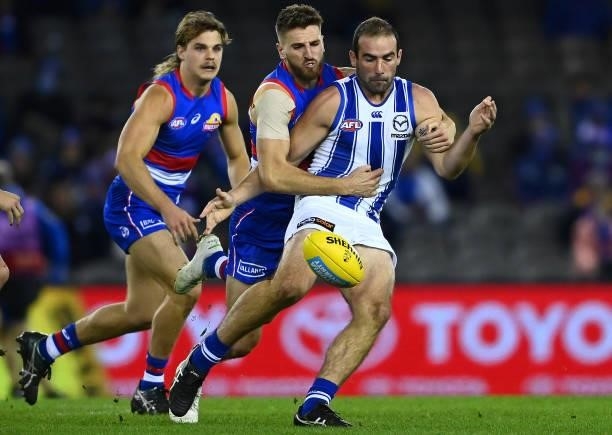 Ben Cunnington of the Kangaroos kicks whilst being tackled by Marcus Bontempelli of the Bulldogs during the round 16 AFL match between Western...