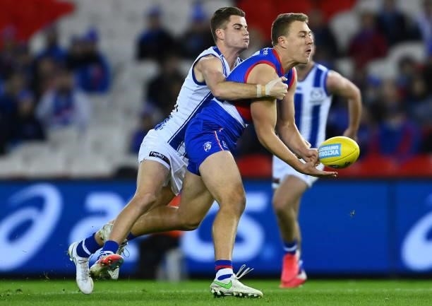Jackson Macrae of the Bulldogs handballs whilst being tackled by Bailey Scott of the Kangaroos during the round 16 AFL match between Western Bulldogs...