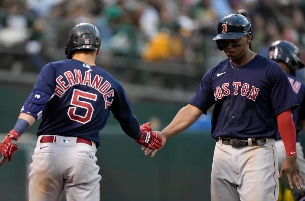 Rafael Devers of the Boston Red Sox is congratulated by Enrique Hernandez after Devers scored against the Oakland Athletics in the top of the 12th...