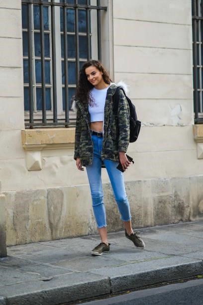 Model wears a white crop-top, a khaki brown and green military print pattern hoodie with white fur long puffer jacket, blue faded denim jeans ripped...