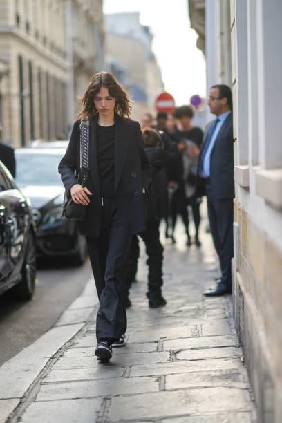 Model wears a black t-shirt, a black blazer jacket, black large pants, a black shiny grained leather Bobby handbag with blue and beige Dior Oblique...