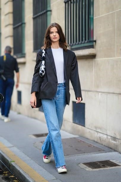 Model wears a white t-shirt, a black blazer jacket, a black and white cow print pattern fluffy shoulder bag, blue faded denim jeans ripped pants,...