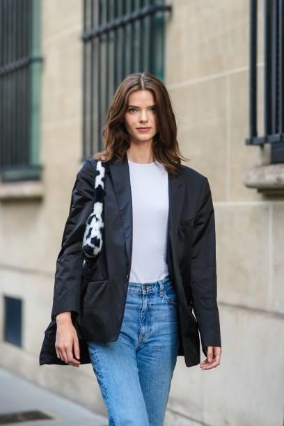 Model wears a white t-shirt, a black blazer jacket, a black and white cow print pattern fluffy shoulder bag, blue faded denim jeans ripped pants,...