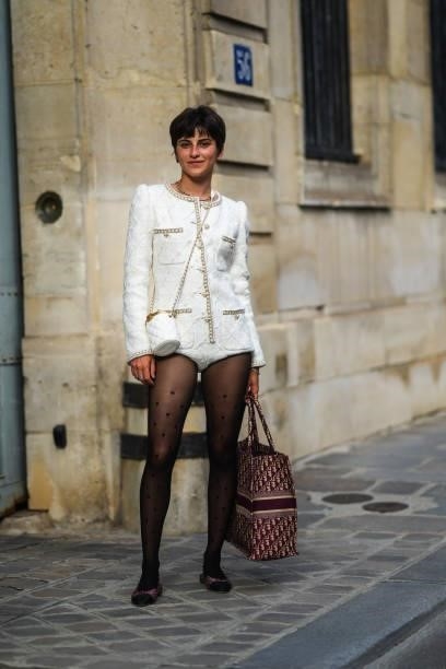 Guest wears necklaces, a white quilted tweed with white leather and gold iconic Chanel chain on the borders jacket bodysuit from Chanel, a white...