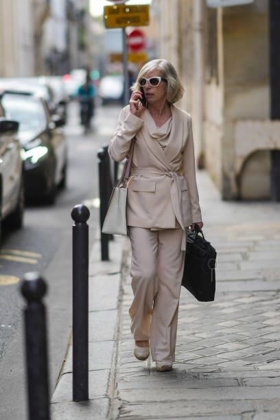 Guest wears white vintage sunglasses, a beige t-shirt, a beige belted silk blazer jacket, matching beige flowing pants, a white matte grained leather...