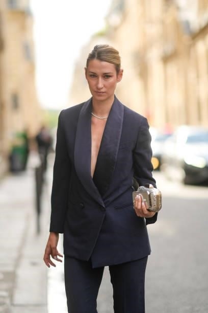 Guest wears a navy blue blazer jacket, matching navy blue suit pants, a silver rhinestones necklace, a silver shiny leather crocodile pattern clutch,...