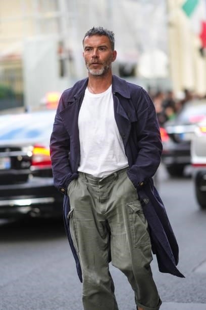 Guest wears a silver necklace, a white t-shirt, a navy blue long coat, khaki cargo large pants, outside Armani, during Paris Fashion Week - Haute...