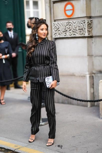Guest wears blue stones pendant earrings, a black silk ribbon in the hair, a black with white stripes zipper belted blazer jacket, matching black...