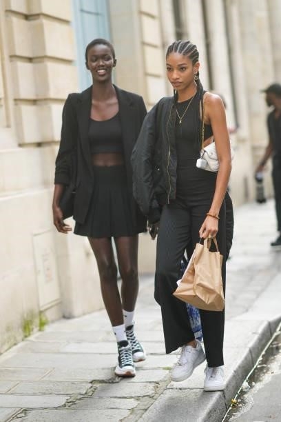 Model wears a black crop-top, a black blazer jacket, a black pleated short skirt, white ribbed socks from Nike, black sneakers from Converse All...