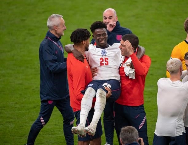Tyrone Mings and Conor Coady of England pick up team mate Bukayo Saka after the UEFA Euro 2020 Championship Semi-final match between England and...