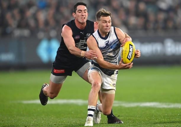 Shaun Higgins of the Cats handballs whilst being tackled by Jacob Weitering of the Blues during the round 17 AFL match between Carlton Blues and...
