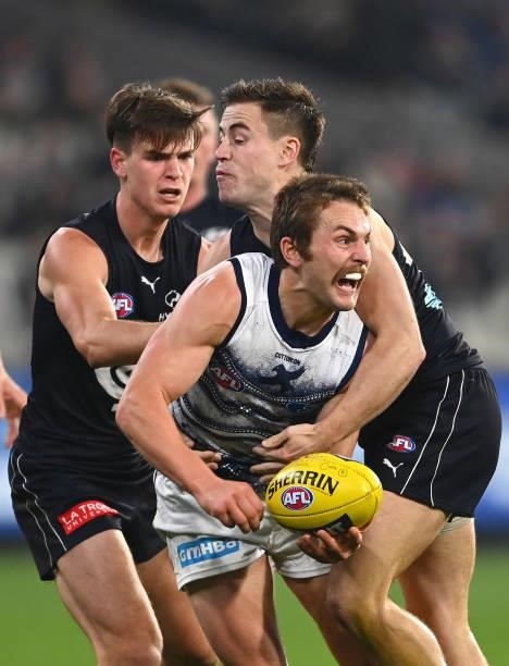 Tom Atkins of the Cats handballs whilst being tackled by Matthew Owies of the Blues during the round 17 AFL match between Carlton Blues and Geelong...