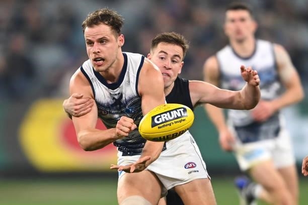Jake Kolodjashnij of the Cats handballs whilst being tackled by Matthew Owies of the Blues during the round 17 AFL match between Carlton Blues and...