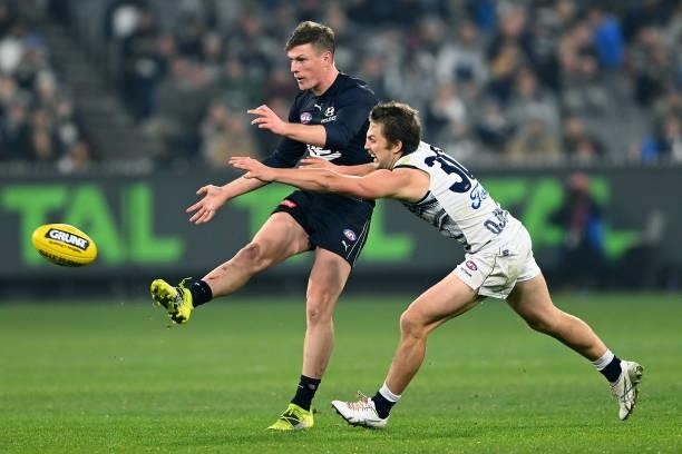 Jack Newnes of the Blues kicks whilst being tackled by Tom Atkins of the Cats during the round 17 AFL match between Carlton Blues and Geelong Cats at...