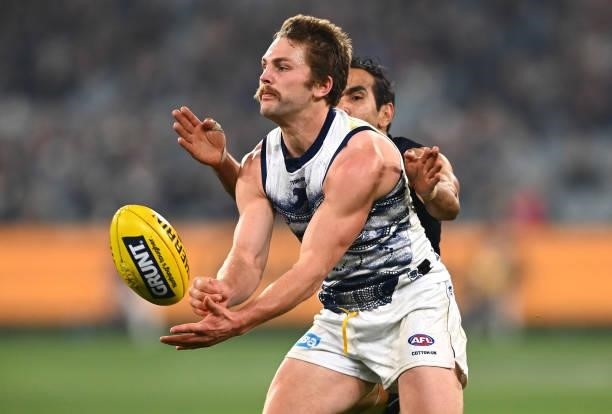 Tom Atkins of the Cats handballs whilst being tackled during the round 17 AFL match between Carlton Blues and Geelong Cats at Melbourne Cricket...