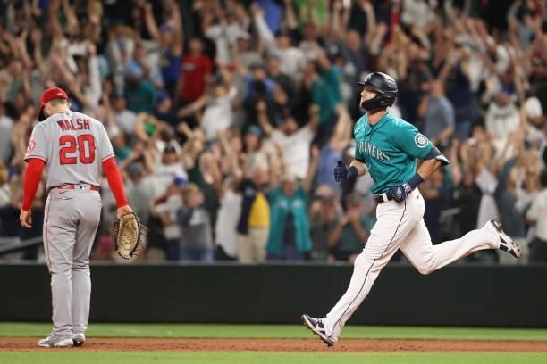 Mitch Haniger of the Seattle Mariners laps the bases alongside Jared Walsh of the Los Angeles Angels after hitting a grand slam to take a 7-3 lead...