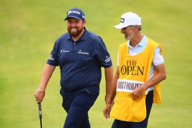 Defending champion Shane Lowry of Ireland smiles with Bryan Drennon, caddie of Louis Oosthuizen of South Africa as they leave the 18th green during...