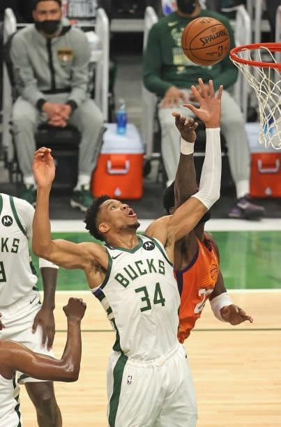 Giannis Antetokounmpo of the Milwaukee Bucks rebounds over Deandre Ayton of the Phoenix Suns at Fiserv Forum on July 14, 2021 in Milwaukee,...