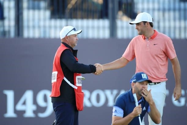 Scottie Scheffler of the United States shakes hands with caddie Scotty McGuinness on the 18th green as Sergio Garcia of Spain prepares to putt during...
