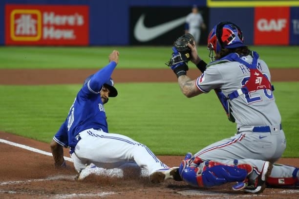 Marcus Semien of the Toronto Blue Jays slides to beat the tag by Jonah Heim of the Texas Rangers on a RBI single by Bo Bichette during the fourth...