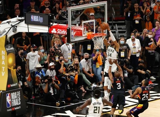 Giannis Antetokounmpo of the Milwaukee Bucks slam dunks the ball over Chris Paul and Mikal Bridges of the Phoenix Suns late in the second half of...