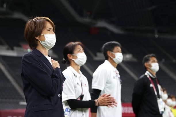 Asako Takakura, Head Coach of Team Japan wears a face mask as they stand for the national anthem prior to the Women's First Round Group E match...