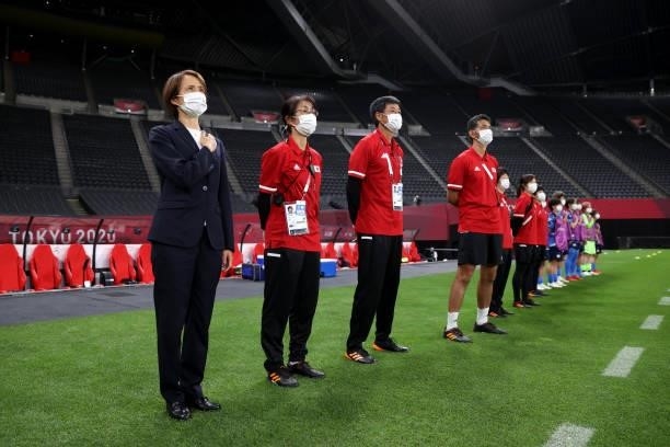 Asako Takakura, Head Coach of Team Japan wears a face mask during the national anthem with the backroom staff prior to the Women's First Round Group...
