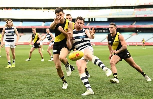 Patrick Dangerfield of the Cats kicks whilst being tackled by Trent Cotchin of the Tigers during the round 19 AFL match between Geelong Cats and...