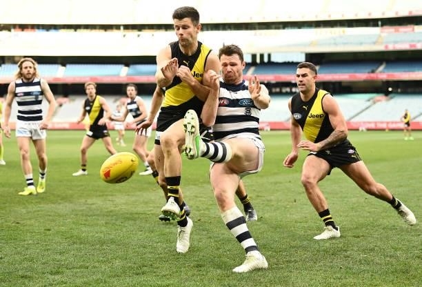 Patrick Dangerfield of the Cats kicks whilst being tackled by Trent Cotchin of the Tigers during the round 19 AFL match between Geelong Cats and...