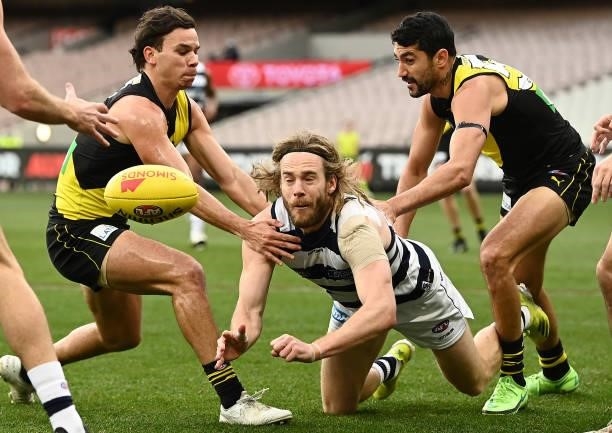 Cameron Guthrie of the Cats handballs whilst being tackled during the round 19 AFL match between Geelong Cats and Richmond Tigers at Melbourne...