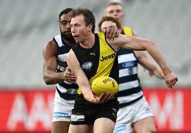 Dylan Grimes of the Tigers handballs whilst being tackled by Esava Ratugolea of the Cats during the round 19 AFL match between Geelong Cats and...