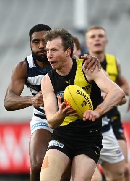 Dylan Grimes of the Tigers handballs whilst being tackled by Esava Ratugolea of the Cats during the round 19 AFL match between Geelong Cats and...