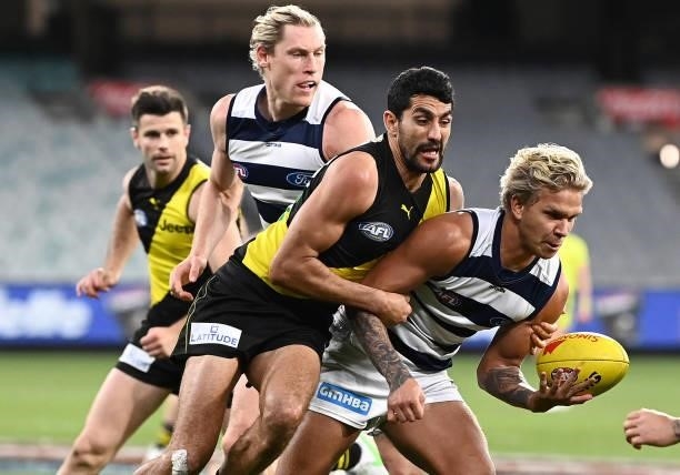 Quinton Narkle of the Cats handballs whilst being tackled by Marlion Pickett of the Tigers during the round 19 AFL match between Geelong Cats and...