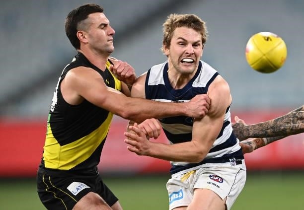 Tom Atkins of the Cats handballs whilst being tackled by Jack Graham of the Tigers during the round 19 AFL match between Geelong Cats and Richmond...