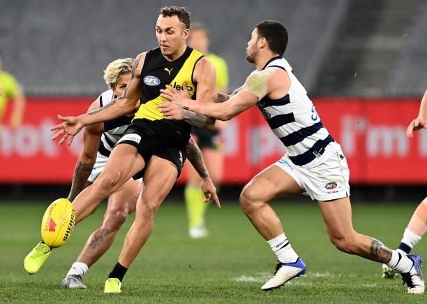 Shai Bolton of the Tigers kicks whilst being tackled by Brandan Parfitt of the Cats during the round 19 AFL match between Geelong Cats and Richmond...