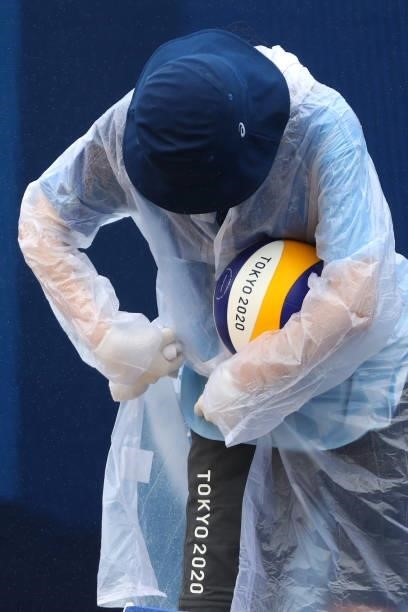 An employee disinfects and attempts to dry a ball during the Women's Preliminary - Pool B beach volleyball match between Team United States and Team...