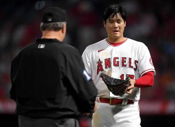 Shohei Ohtani of the Los Angeles Angels smiles at the umpires waiting to check his glove and hat after the sixth inning of the game against the...