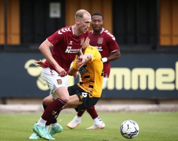 Mitch Pinnock of Northampton Town moves with the ball past Harvey Knibbs of Cambridge United during the Pre Season Friendly match between Cambridge...