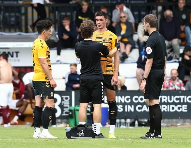 Lloyd Jones of Cambridge United receives treatment as George Williams and Referee Alan Dale look on during the Pre Season Friendly match between...