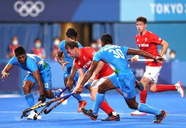 Christopher Griffiths of Team Great Britain runs with the ball whilst being challenged by Varun Kumar and Amit Rohidas of Team India during the Men's...