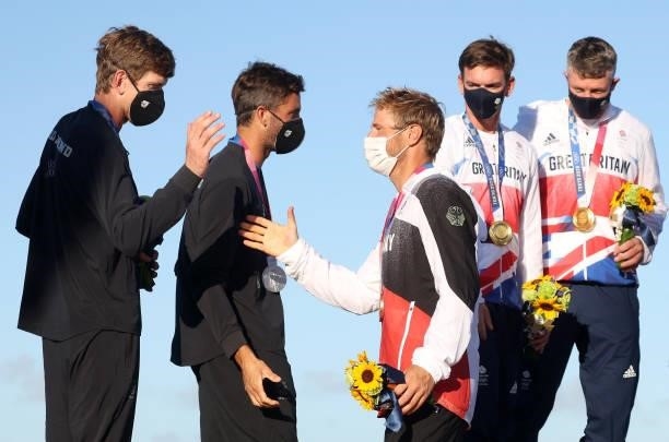 Peter Burling and Blair Tuke of Team New Zealand greeted by Erik Heil of Team Germany on the podium after receiving their medals for the Men's Skiff...