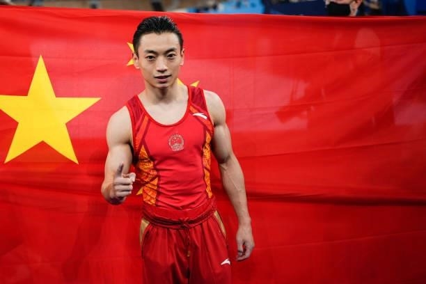 Gold medalist Zou Jingyuan of Team China celebrates in front of a Chinese national flag after the Men's Parallel Bars Final on day eleven of the...