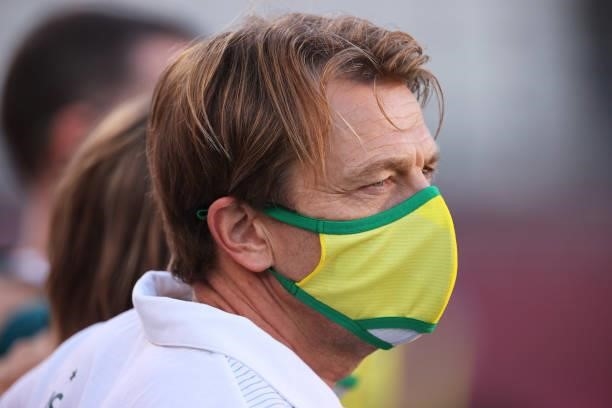Tony Gustavsson, Head Coach of Australia wears a face mask as he sings the national anthem prior to the Women's Bronze Medal match between United...