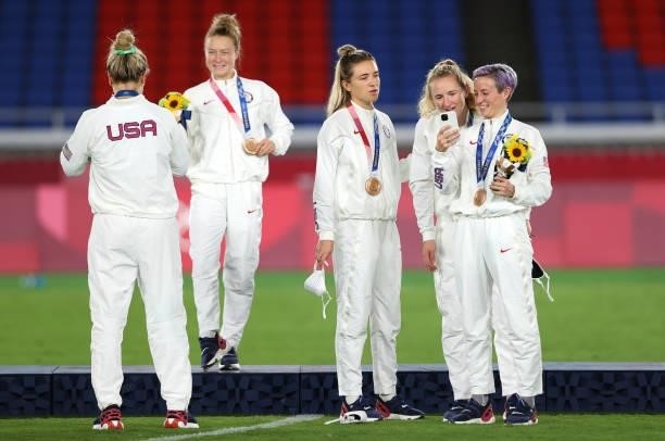 Bronze medalist Megan Rapinoe of Team United States shows her phone to team mate Sam Mewis during the Women's Football Competition Medal Ceremony on...